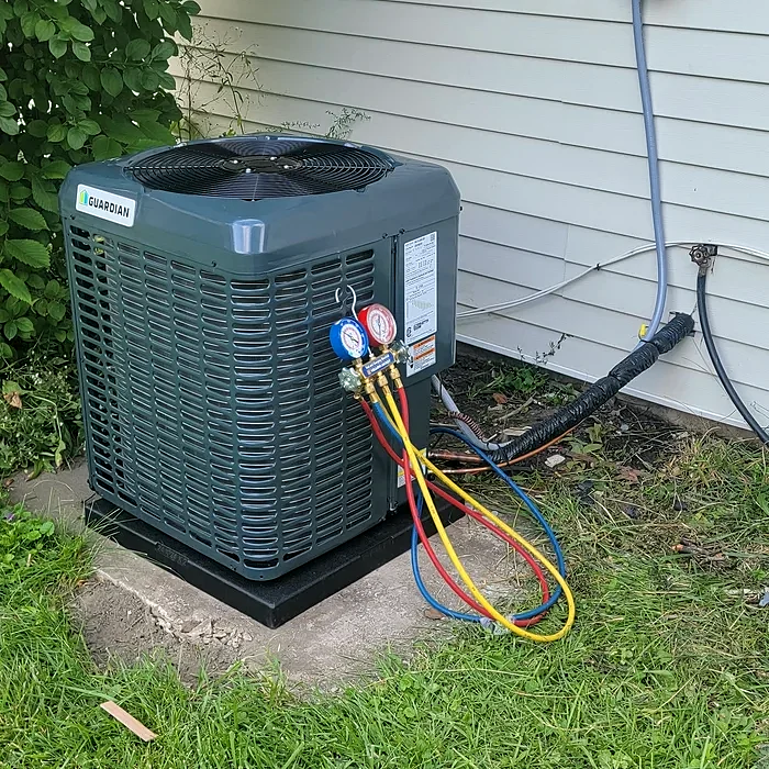 An outdoor air conditioning unit with a technician’s gauge set connected, beside a house