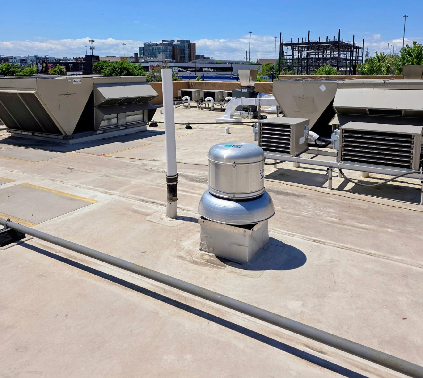 A commercial flat roof with large rooftop air handling units, a stainless steel exhaust fan and a vent pipe