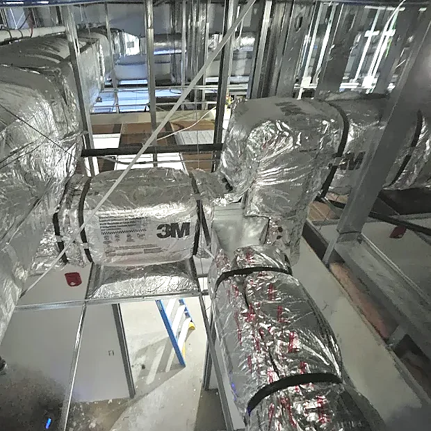 Foil-wrapped insulated ducts running through the ceiling of an unfinished building