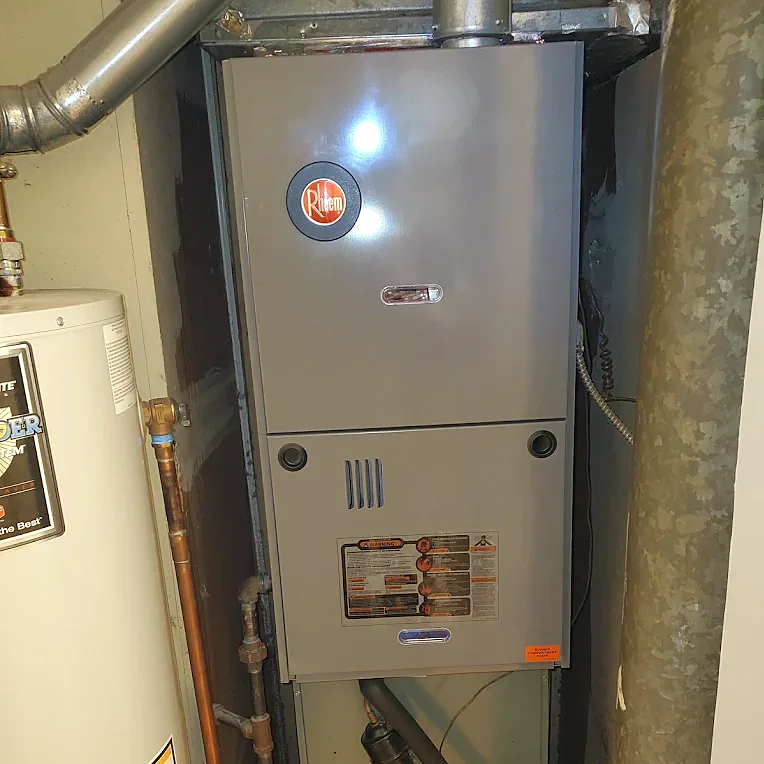 A furnace installed in a closet beside a water heater, with copper and iron piping and a metal flue above