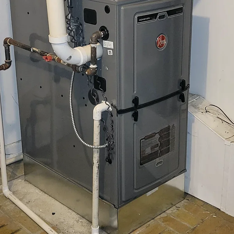 A furnace in a utility room with white PVC vent pipes, a gas line and flexible electrical conduit connected