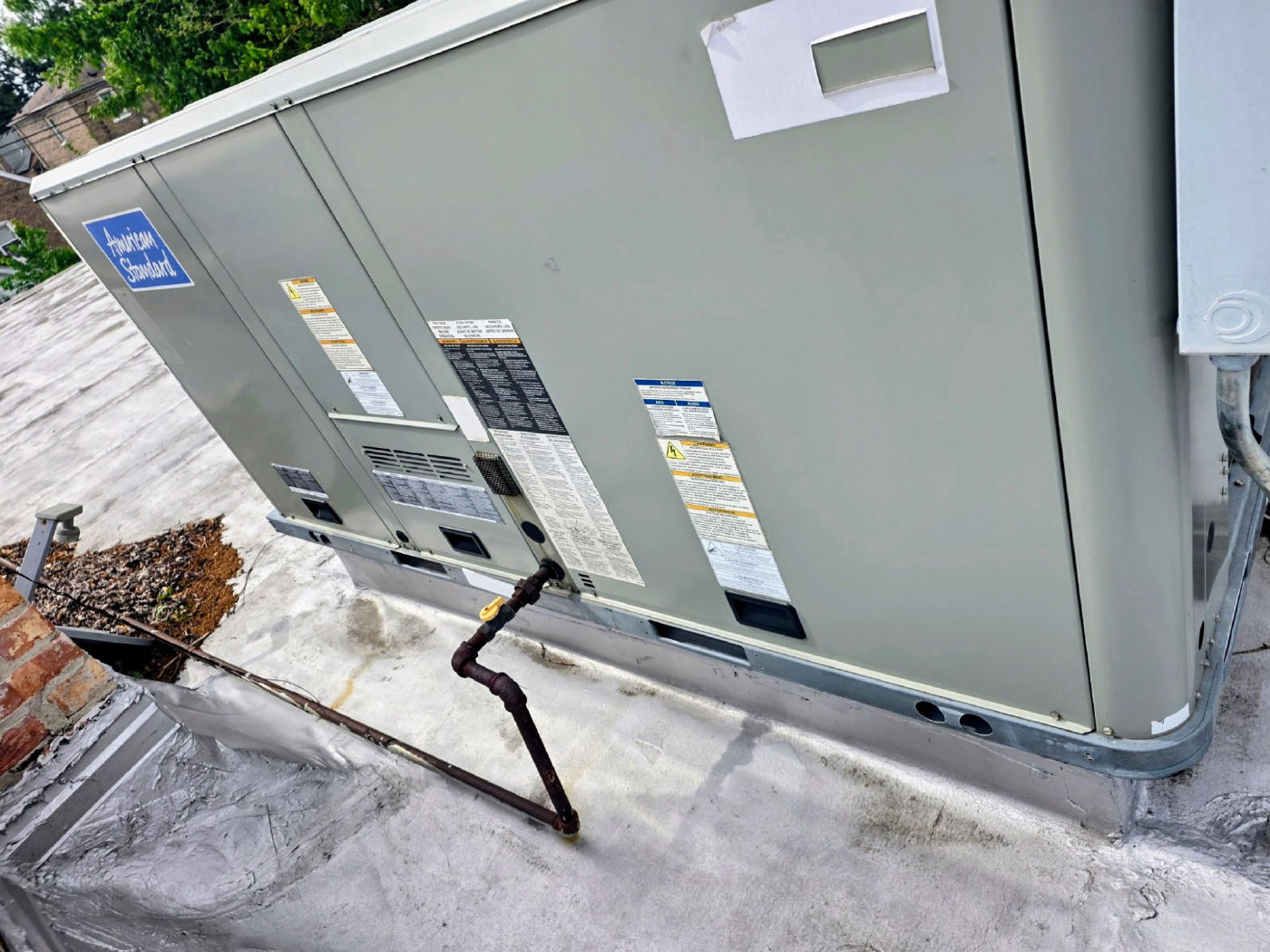 An American Standard rooftop packaged unit on a flat roof, with its gas line and shutoff valve