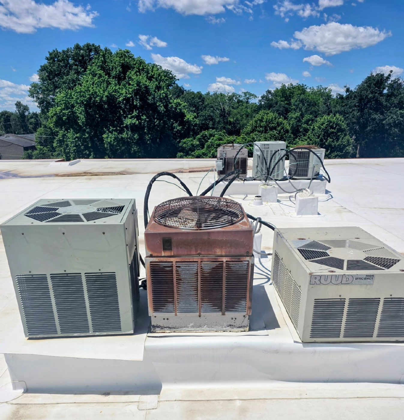 Three older air conditioner condenser units on a flat white commercial roof, with more units behind them