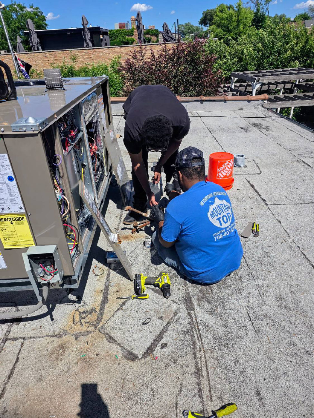 Two technicians working on a rooftop packaged unit with its panel open, showing the wiring and refrigerant piping
